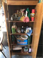 Photo of open wooden cabinet showing three shelves filled with assorted cleaning and household items.