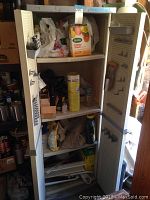 Full view of the open grey plastic cabinet filled with various used gardening supplies like plant food, spray cans, gloves, and packets.