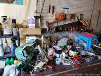 Workbench surface with bench grinder, small vise, hand tools on pegboard, various small hardware and supplies scattered around.