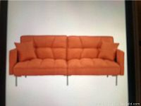 Front view of bright orange split back futon with tufted upholstery and two matching pillows.