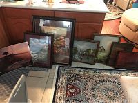 Seven framed landscape prints arranged leaning against wood cabinet and appliances, size range visible, varying frame styles