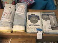 Two rolled sets of curtains with white to yellow ombre, packaged with labels and light filtering box showing design solution brand