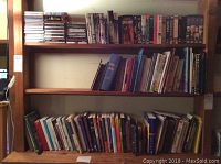 Three shelves holding a variety of CDs, books, DVDs, and VHS tapes in mixed order.