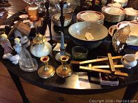 Photo of various items on a table including blue bowl with crack and chip, gold electroplated candle holders, bronze candlestick, and other small decorative items.