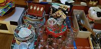 View of Christmas themed plates, glassware, small knives in wooden holder, and house-shaped baking pan among other kitchen items.