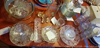 Overview of clear glass, crystal, and cut glass items on a table including bowls, plates, cups, and small decorative dishes.