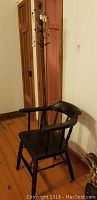 Vintage wooden chair with curved spindled back and painted finish next to tall wooden coat rack