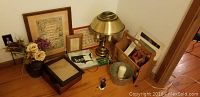 Lot items arranged on wooden floor including brass lamp, framed wall art, vase with flowers, tin pail, magazine rack, and candle holder