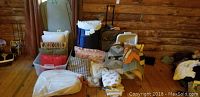 Full view of lot with quilts, pillows, and storage tubs on wooden floor in front of log wall.