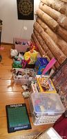 Photo showing a variety of kids toys including puzzles, toy banks, and novelty items arranged on a wooden floor next to a wall with log design, with a roll-up dart board hanging above.