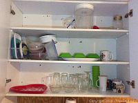 View of cabinet with glass drinking glasses, bowls, plastic containers, mugs, and green silicone ramekins.
