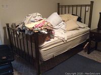 Brass bed frame with mattress and box spring covered in linens and pillows, showing headboard.