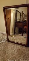 Full view of the framed mirror standing on carpeted floor, showing the barrel style wooden frame and reflective glass surface.