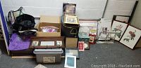 Wide angled photo showing entire lot with framed art, storage boxes, totes, and other items on a floor.