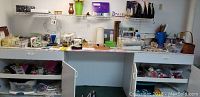 Full view of a white crafting cabinet filled with assorted scrapbooking and crafting supplies including ribbons, glue sticks, paints, scissors, papers and tools.