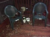 Two green plastic patio chairs with leaves on and around them, set on wooden floor.