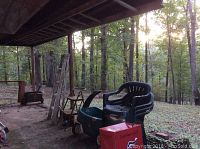 Wide shot showing stacked plastic patio chairs, kids wagon, step stool, and two aluminum ladders under a wooden porch.