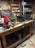 Full view of the wooden workbench with various tools on top and electrical outlets on the front panel.