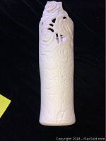 White ceramic vase with detailed rose cutout design photographed on a black background to show texture and detail.