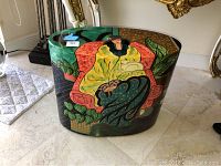 Side view of oval lacquer finished table with a painting of a woman in yellow and green attire, a plant, and abstract patterns.