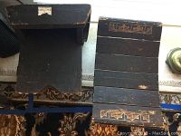 Top and bottom view of two black wooden stools showing paint chipping, carved decoration on one end, and overall wear.