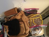 Leather tan backpack overview with black crochet bag and plastic tote bag in view, along with miscellaneous items in plastic bags.