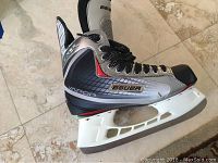 Side view of single Bauer Vapor ice hockey skate showing silver and black synthetic construction, black laces, white blade holder and stainless steel blade.