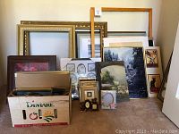 Various framed artwork, prints, and a box with smaller frames and art pieces, showing the lot contents.