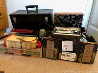 Multiple radios, speaker panel, 8-track player and case packed in cardboard trays and black vinyl case