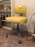 Yellow vinyl and steel rolling office chair with adjustable height photographed at an angle showing seat and backrest.