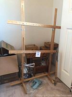 Wooden quilt frame with adjustable crossbars and legs standing in corner