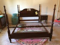 Full cherry wood queen bed frame assembled, showing headboard, footboard with finials, and side rails on patterned rug.