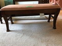 Front view of the wooden bed bench showing the carved legs and upholstered seat with signs of wear.