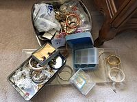Full view of the assorted vintage costume jewelry in a metal tin including bangles, faux pearl jewelry, clip-on earrings, and chains.