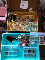 Top view of box with assorted vintage costume jewelry including necklaces, bracelets, and brooches on a yellow satin-like fabric base.