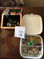 Photo of the copper jewellery box alongside a white plastic divided container filled with assorted costume jewellery pieces including brooches and earrings.