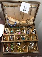 Full view of wooden jewellery box with the lid open showing hanging necklaces and multiple compartments filled with assorted vintage costume jewellery including brooches, pins, earrings, and rings.
