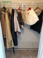 Overall closet shot showing tan and black coats, fur collar, white fur stole, metal belt, and black beaded top hanging on wire rack
