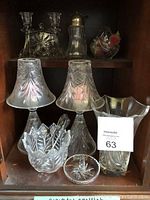 Photo of crystal and glass items inside a cupboard showing nine distinct pieces including candle holders, decorative bowls, a silver-topped bottle, and vases.