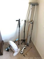 Photo of homecare items including Easy Cycle pedal exerciser, walking canes, crutches, and pull bar leaning against a white wall