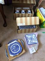 Striped cardboard boxes containing new-in-box cups and loose plates on carpet