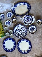 Full view of plates, cups, bowls, and platter arranged on floor showing blue and white transferware ceramic pieces with decorative patterns.