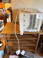 Mainstays window air conditioner placed on wooden shelving unit showing side vents and power cord.