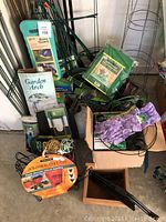 Lot contents including garden arch, kneeler pad, adjustable plant risers, tomato cages, and garden gloves.