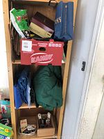 Photo of wooden shelving with red Kandy Premium Melons box containing rodent traps and cans above, tarps on middle shelf, and small items below