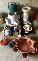 Side view of assorted pots, planters, watering cans, and a decorative garden stand with floral carvings.