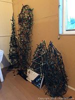 Photo showing multiple lighted wire-frame Christmas decorations including tall 3D trees and triangular trellises, wires and bulbs visible wrapped over frames.