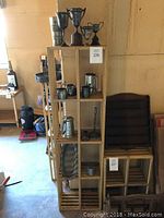 Full view of wooden shelf with metal trophy cups, cream and sugar sets, candle holders, beer steins, and other metal items.