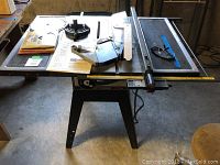 Craftsman 10-inch table saw on stand with various accessories laid out on saw surface including blade guards and fences.