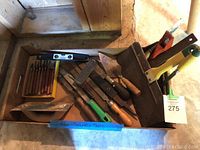 Photo showing a variety of hand tools including wood carving knives, files, trowels, a spirit level, and a metal box with a handle.